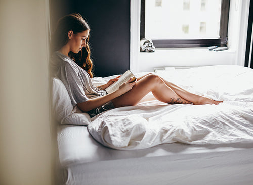 Young woman reading a book in bedroom