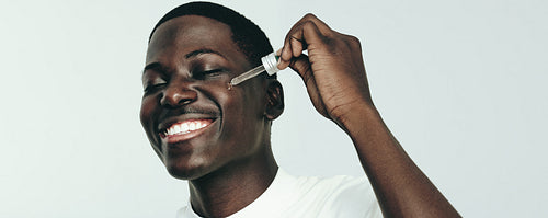 Proud of his skincare routine, young man applies beauty oil on his face