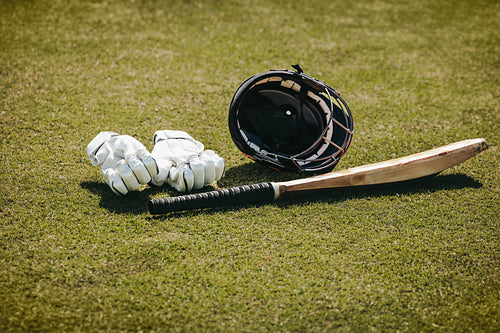 Cricket equipment including bat, helmet and gloves resting on a grassy field