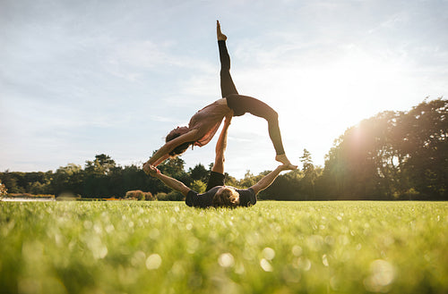 Young couple doing acrobatic yoga on lawn