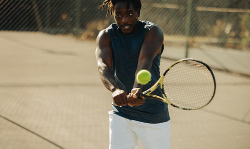 African-American man playing tennis on outdoor court with focus and intensity
