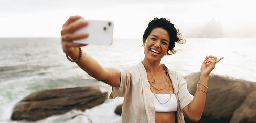 Woman pointing and smiling while taking a selfie on a seaside vacation