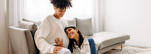 Lesbian mother-to-be listening to her unborn baby kicking