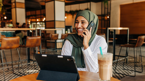Happy Muslim businesswoman taking a phone call in a cafe