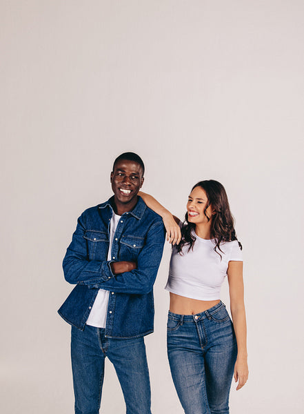 Denim-dressed couple smiles as they stand together in a studio setting