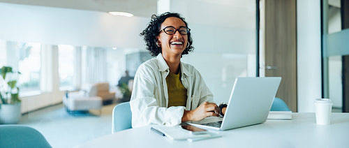 Woman laughs while working on laptop in office.
