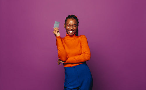 Happy young woman paying with contactless card on vibrant purple background
