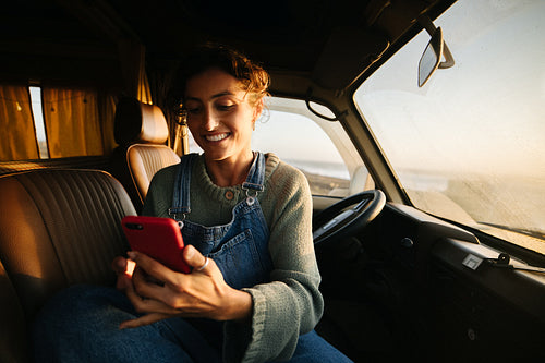 Woman in camper van smiling while using smartphone
