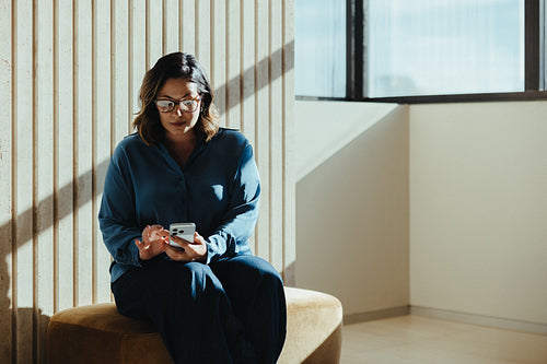 Businesswoman uses her smartphone while sitting in a modern office waiting area