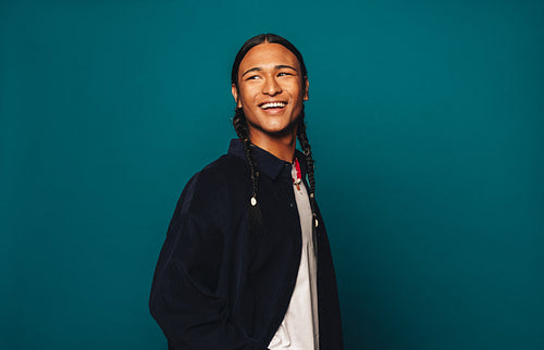 Cheerful ethnic man with braided hair standing on blue background