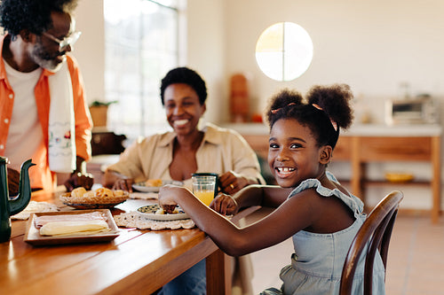 Afro-brazilian girl enjoying a cheese bread rolls breakfast with her parents at home