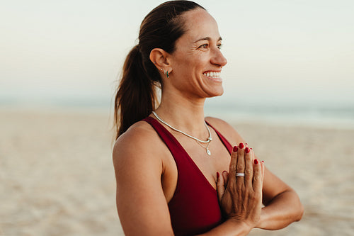 Smiling woman meditating on a serene beach during a calm sunset
