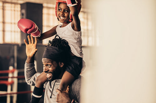 Smiling boxer kid sitting on the shoulder of his trainer