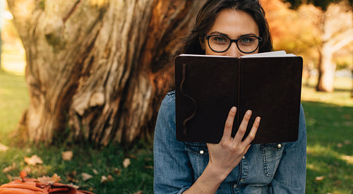 Woman peeking over a book at park