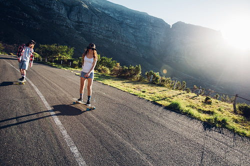 Two young people skating outdoors on rural road