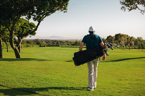 Man walking on golf course carrying golf clubs at a resort