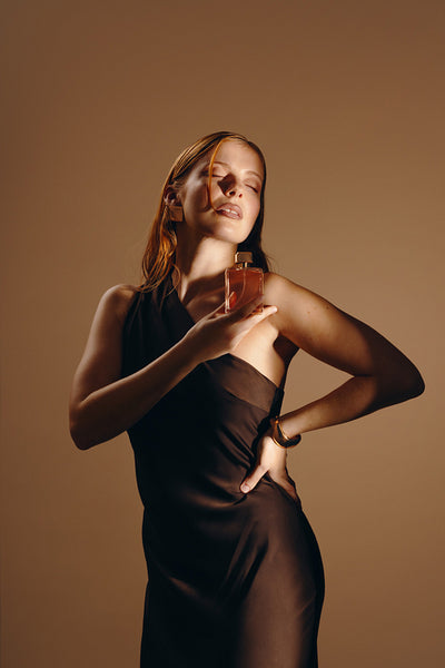 Elegant woman holding perfume bottle against her chest