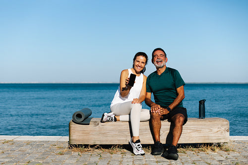 Senior man and woman relaxing by the water with yoga gear and smiles