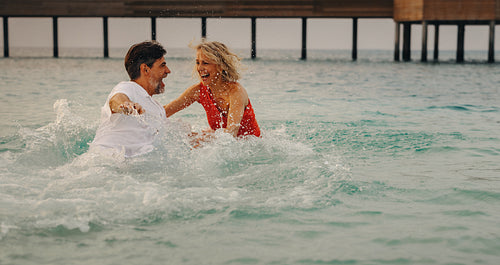 Tropical vitality: Playful retired couple embracing happiness, splashing in the ocean