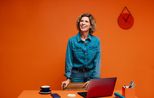 Confident female manager using laptop in a bold orange contemporary office space