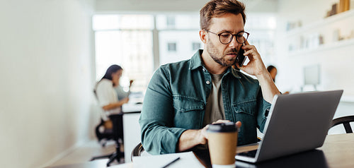 Male designer making a phone call to a client in an office