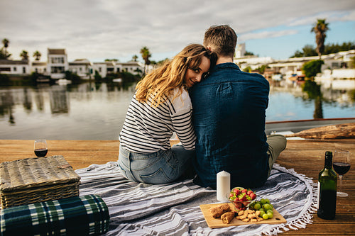Romantic couple on a date sitting near a lake with snacks