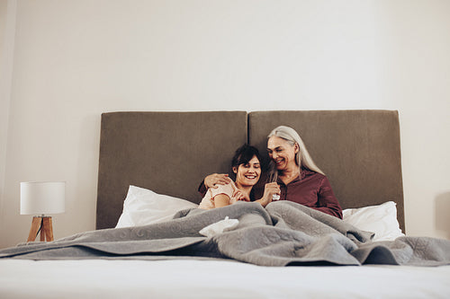 Happy mother and daughter sitting together on bed at home