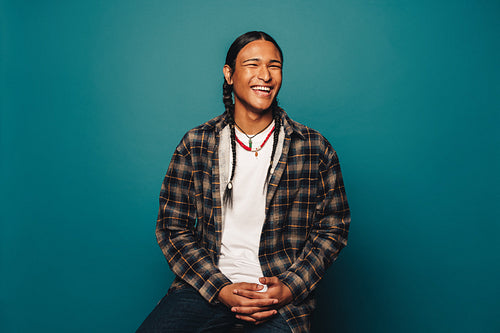 Happy young man with braided hair and ethnic jewelry on blue background