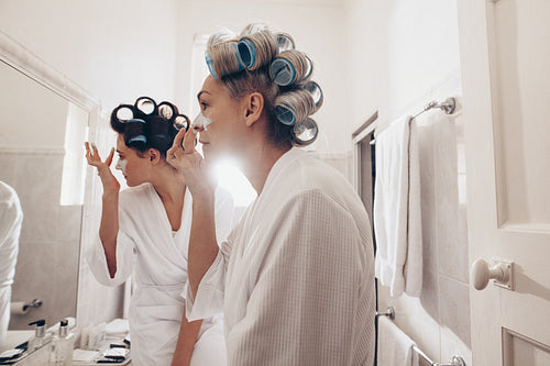 Happy mother and daughter applying face cream standing in the bathroom