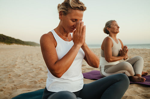Women practicing yoga on a serene beach during a tranquil sunrise
