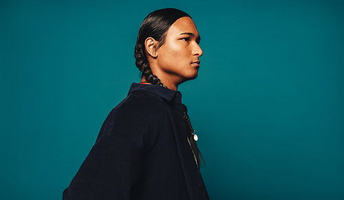Native man with long braided hair standing against a blue studio background