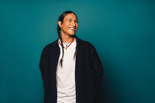 Happy young man with braided hair and ethnic jewelry standing on blue background