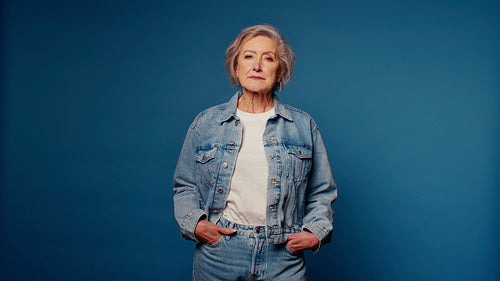 Senior woman in denim poses confidently on blue studio background