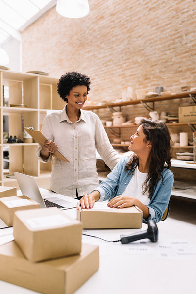 Happy female entrepreneurs smiling at each other in a warehouse