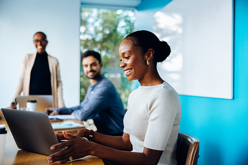 Businesspeople discussing in an office setting with focus on woman using laptop