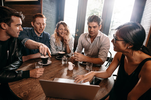 Group of young friends sitting at cafe with laptop