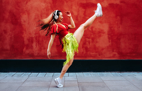Woman dances with headphones outdoors against a red wall