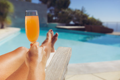 Young lady with orange juice sunbathing at the poolside