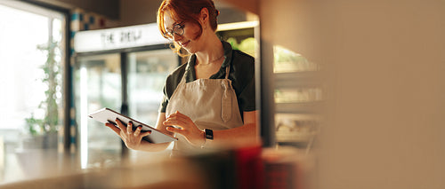 Deli owner managing orders on digital tablet