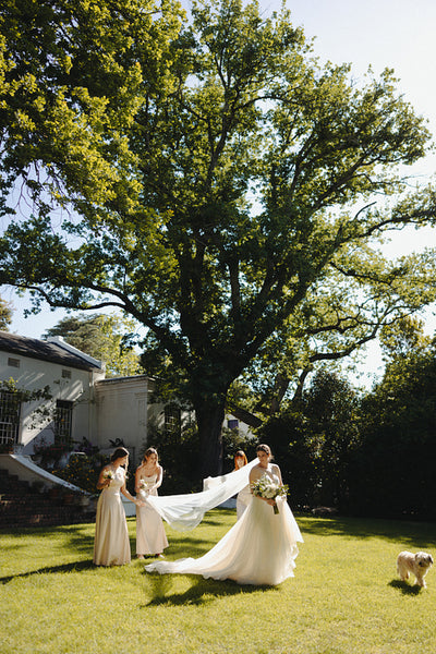 Bride walking with bridesmaids under a large tree in the garden