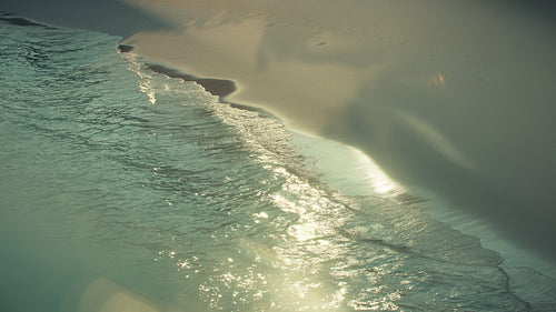 Gentle ocean wave along sandy tropical beach at sunrise