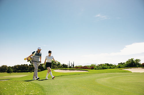 Man carrying female golfer golf clubs walking on fairway enjoying a discussion strategising