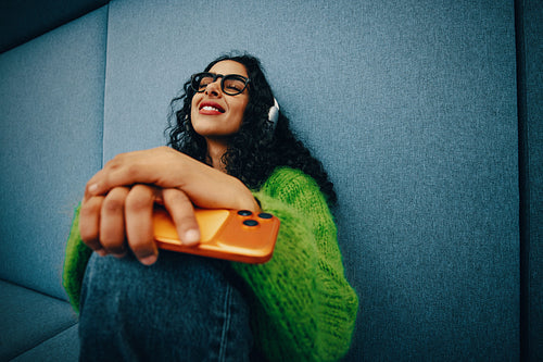 Young woman relaxing with smartphone in work lounge wearing headphones