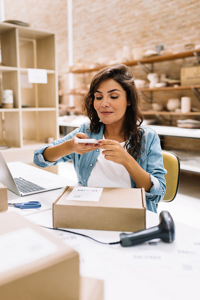 Creative businesswoman taking a picture of a package box in a warehouse