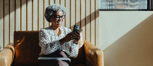 Black mature business woman smiling while using smartphone in a modern lounge
