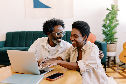 Afro-haired couple enjoying quality time together at home, smiling and browsing on a laptop