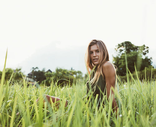Beautiful young woman sitting in the field of tall grass