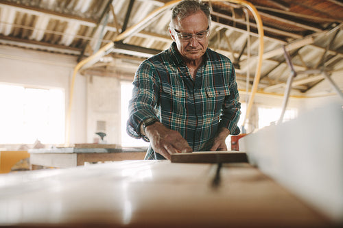 Senior male carpenter working on table saw machine