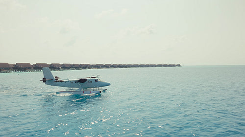 Seaplane taxiing on turquoise ocean near overwater villas at tropical resort