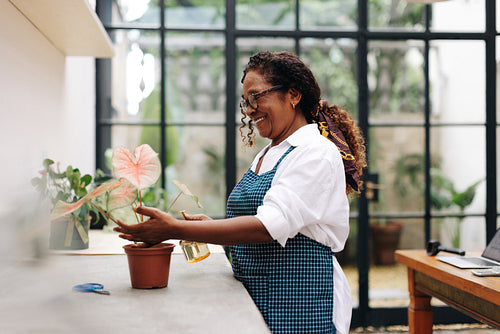 Black female florist smiling as she waters a plant of flowers